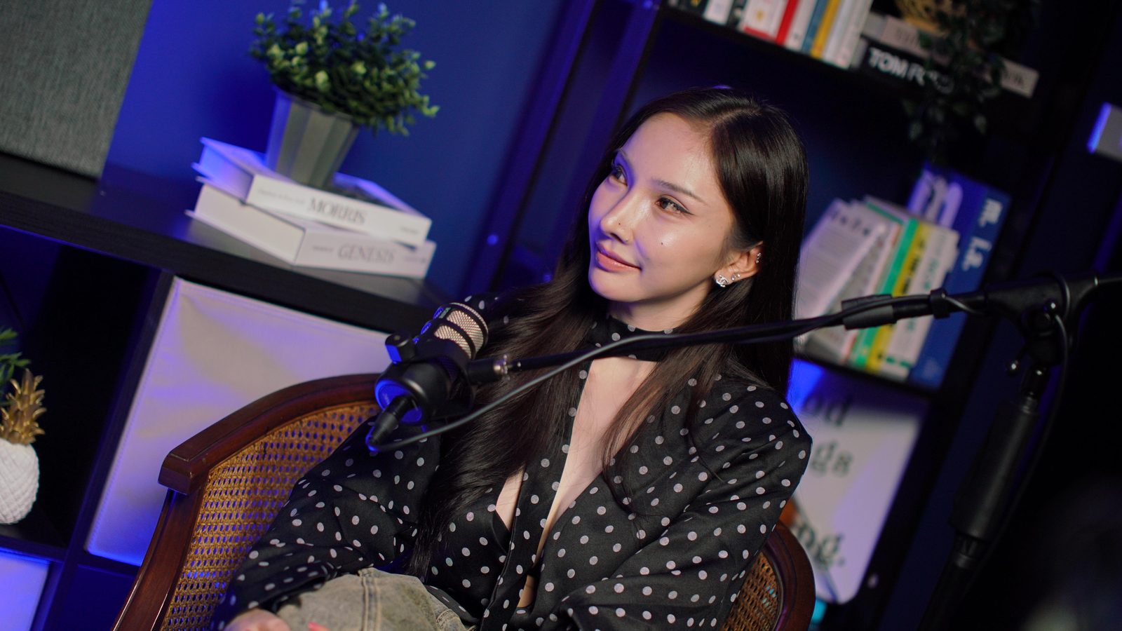 A guest in a polka-dot shirt seated in the cane-back armchair at the New York set, bookshelf behind