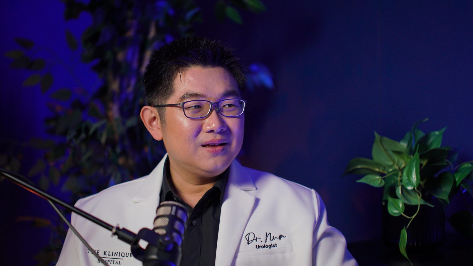 A guest in a white medical coat mid-sentence at the New York set microphone, plants either side