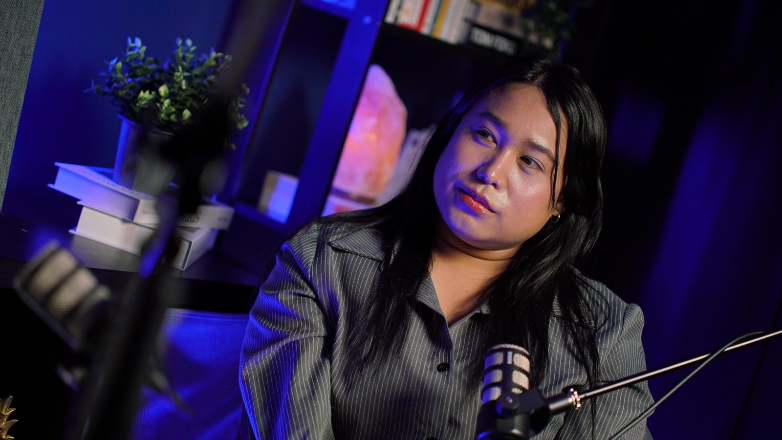 A guest in a pinstripe shirt listening at the New York set, styled shelf and lamp behind her