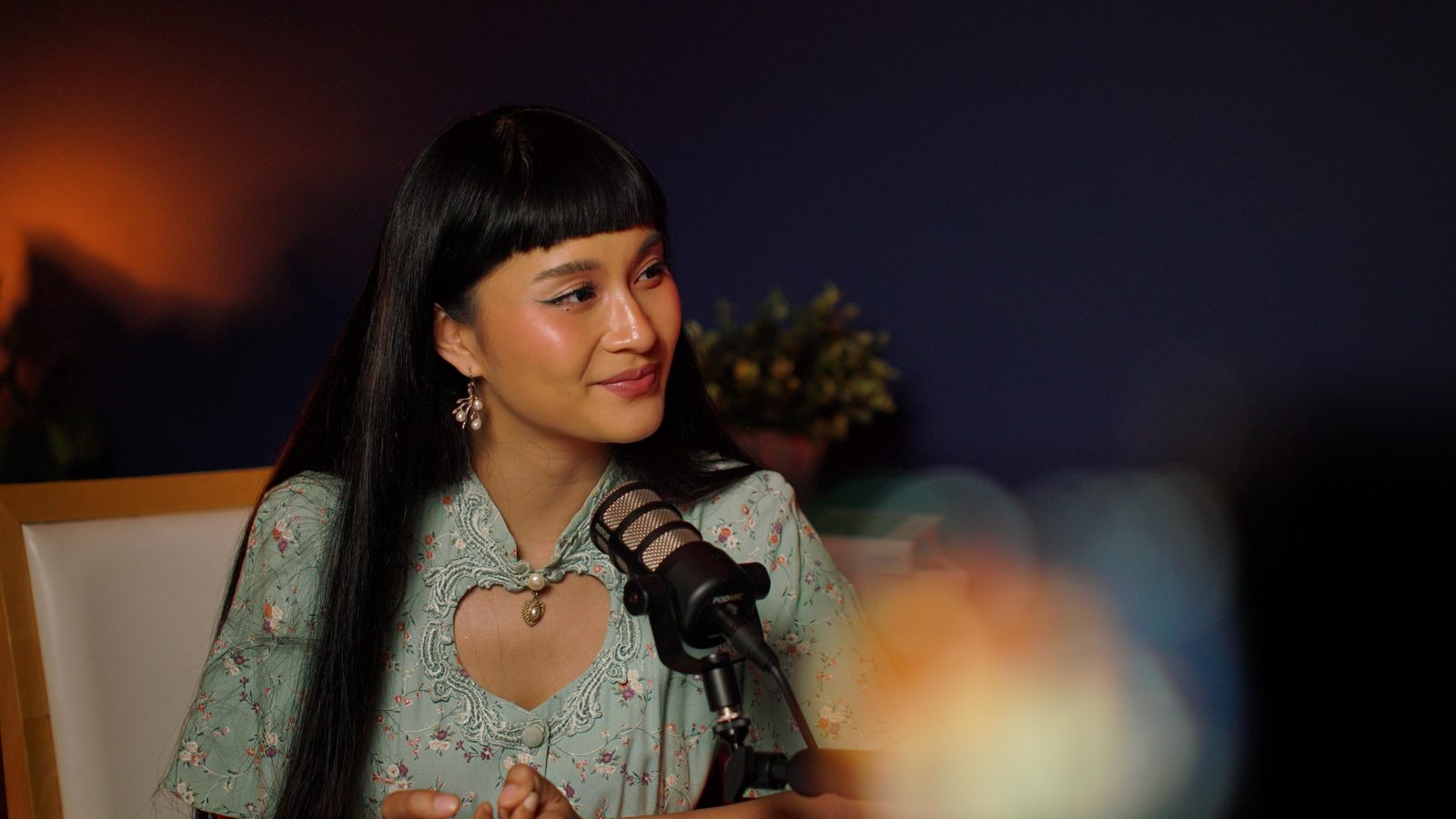 A guest in a floral dress at the Paris set, hands clasped, warm lighting across the navy wall
