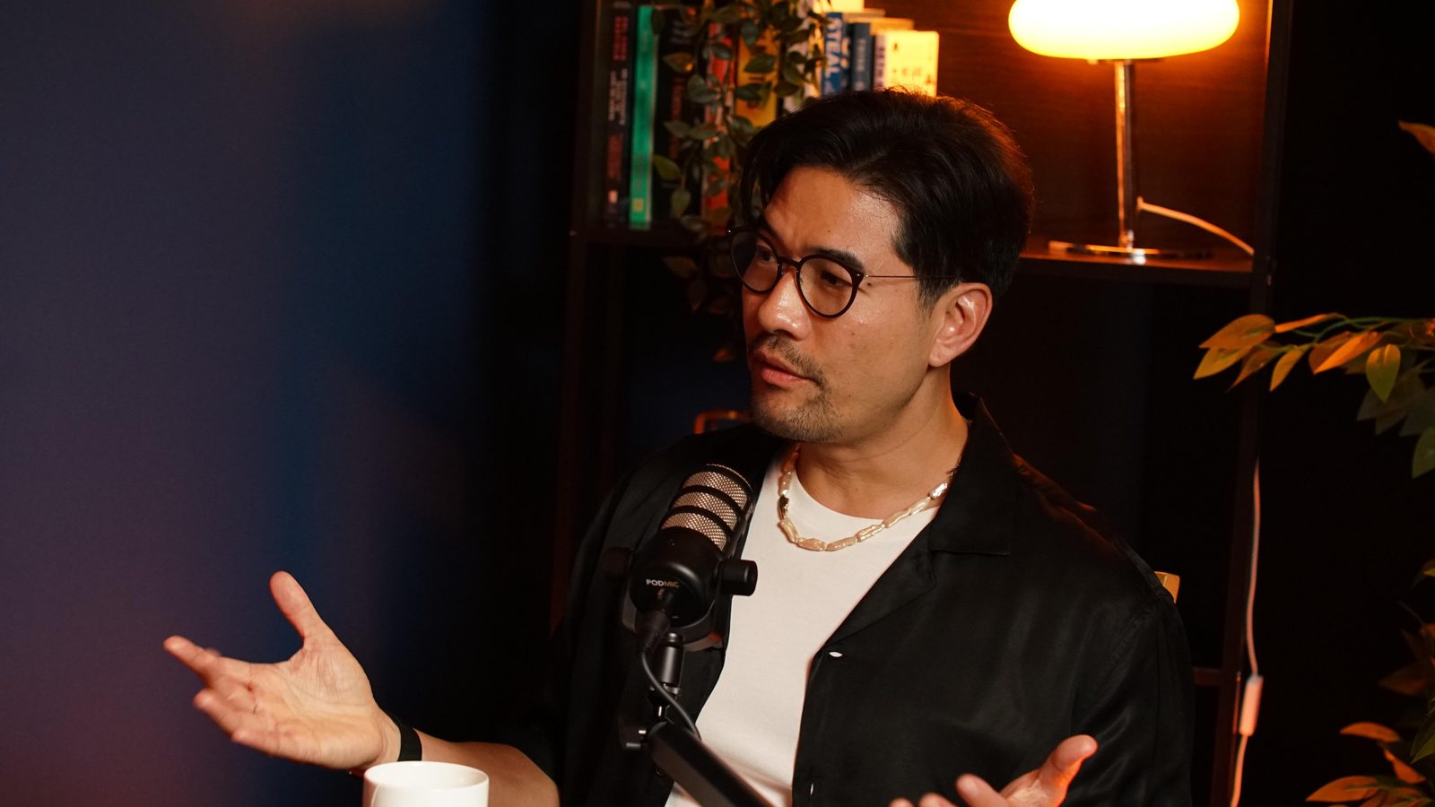A guest in a black shirt gesturing mid-conversation at the Paris set table, mug and mic arm in frame