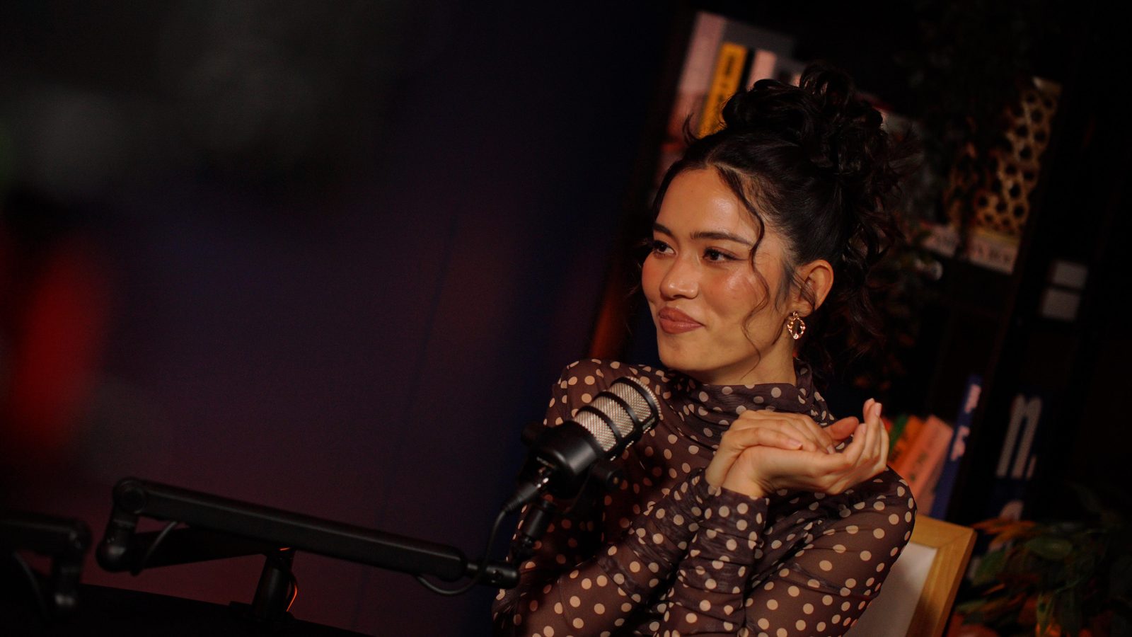 A guest in a polka-dot top smiling at the Paris set, bookshelf and warm side light behind her