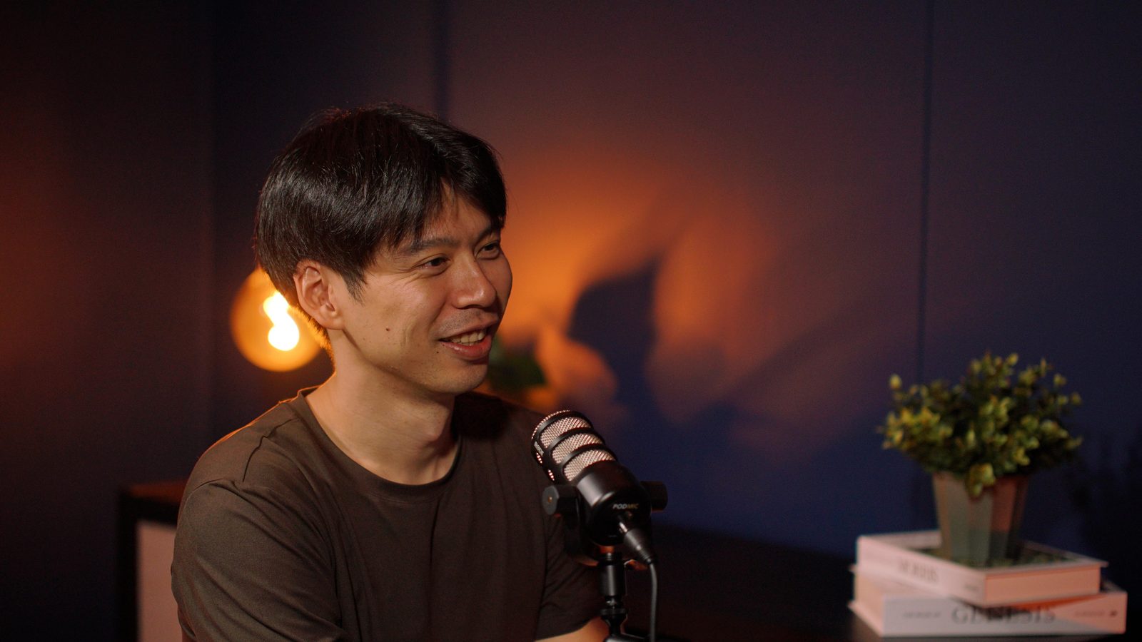 A guest in an olive t-shirt laughing at the Paris set, orange wall light and plant behind him